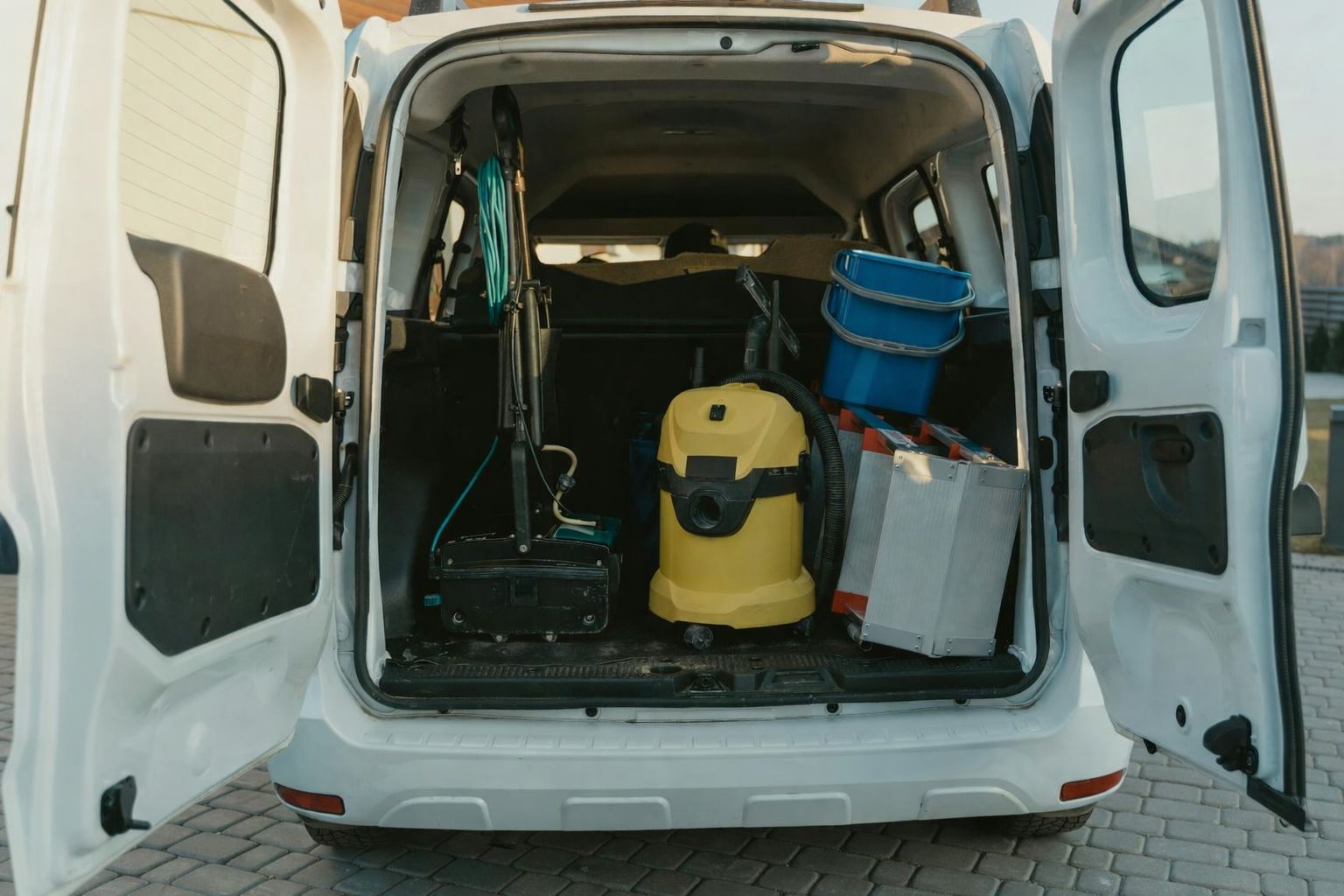Achterkant van een witte bestelwagen vol schoonmaakspullen.
